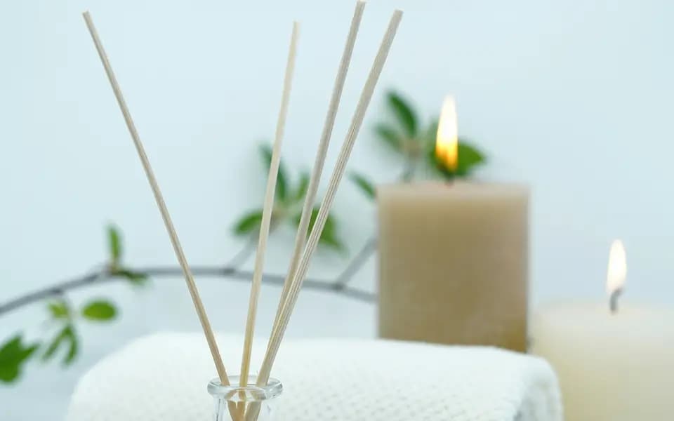 A reed diffuser, candles and a rolled white towel in a calm spa setting
