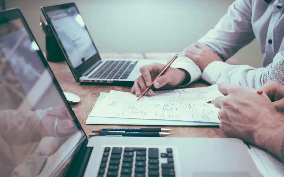 Hands pointing at a plan on paper beside an open laptop