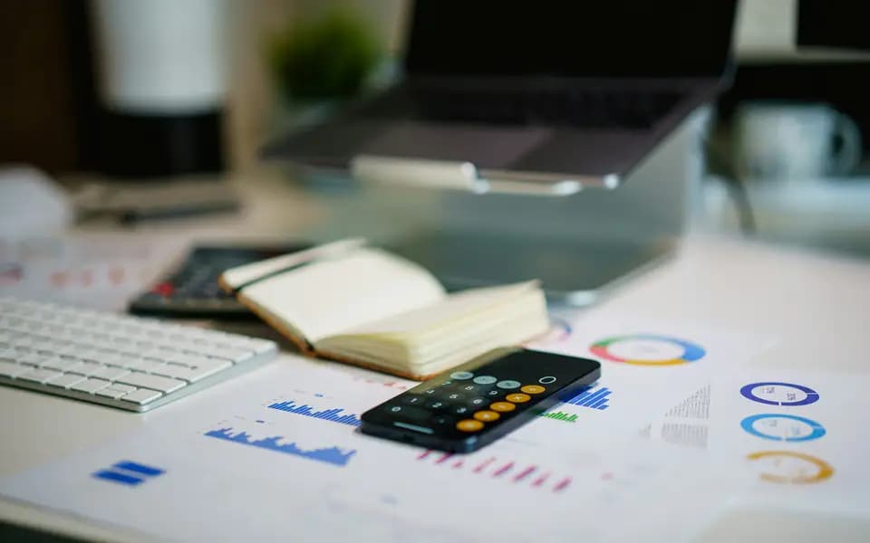 A desk with a laptop, notebook, calculator and printed charts