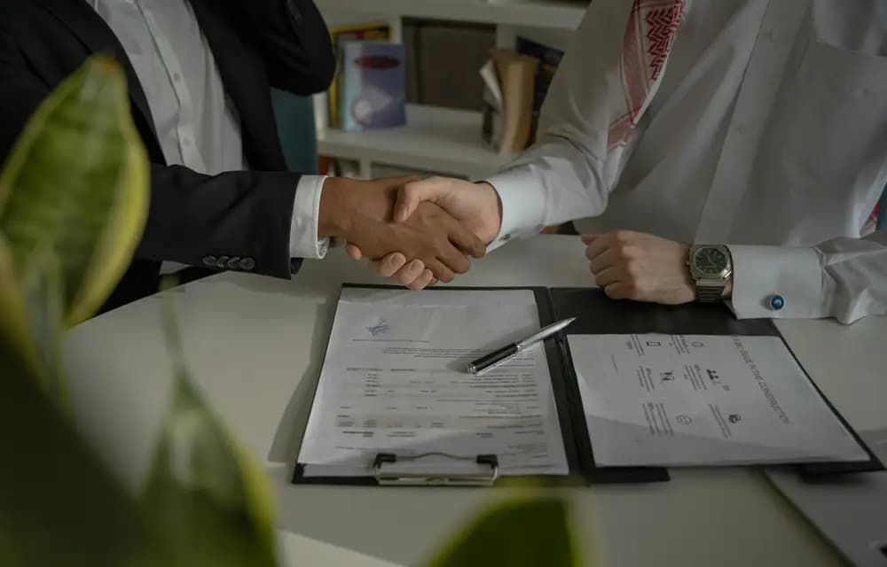 Two professionals shaking hands over signed paperwork