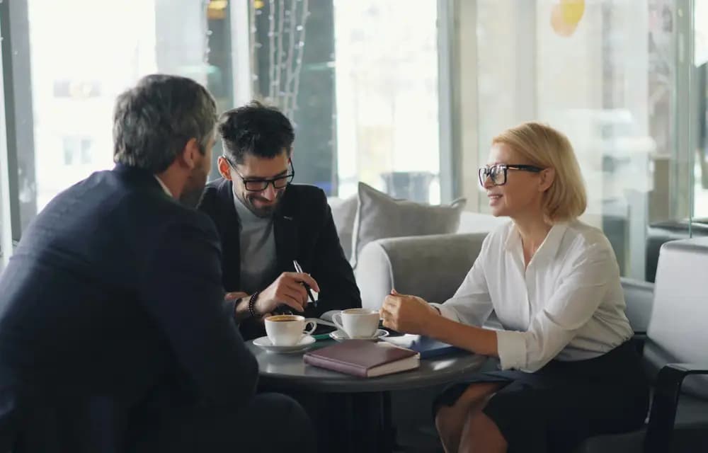 A lawyer talking with two clients over coffee in a bright office