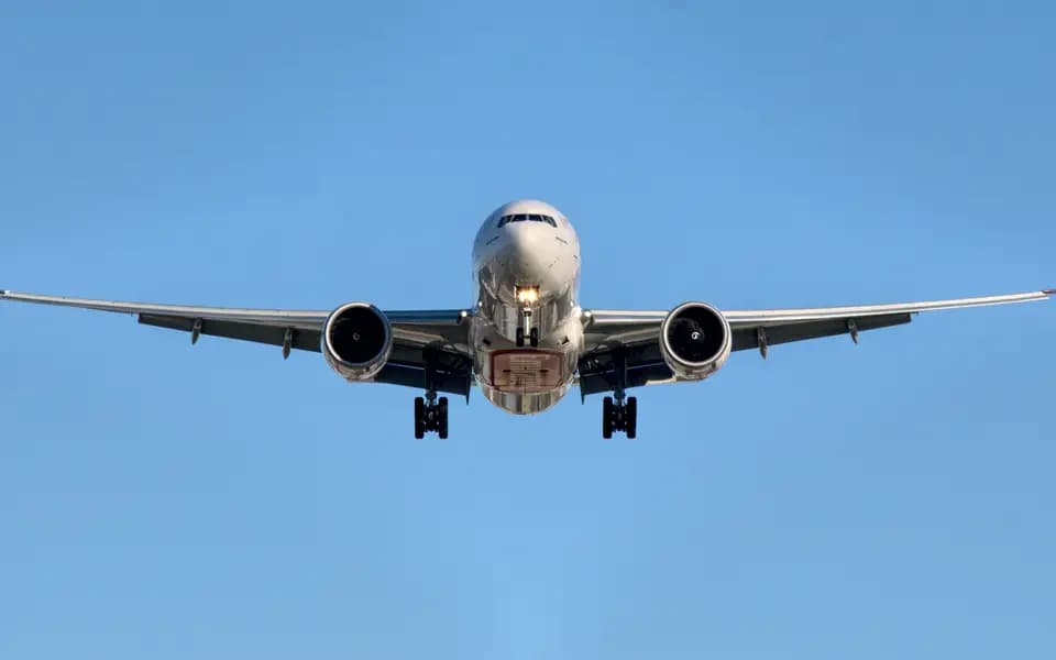 A cargo aircraft flying low with landing gear down against a clear sky