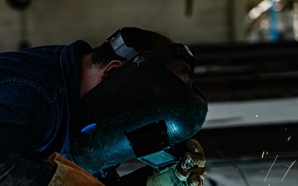 A welder in protective gear working on metal with sparks flying
