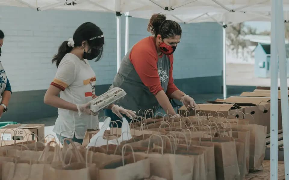Volunteers packing food into paper bags at a distribution event