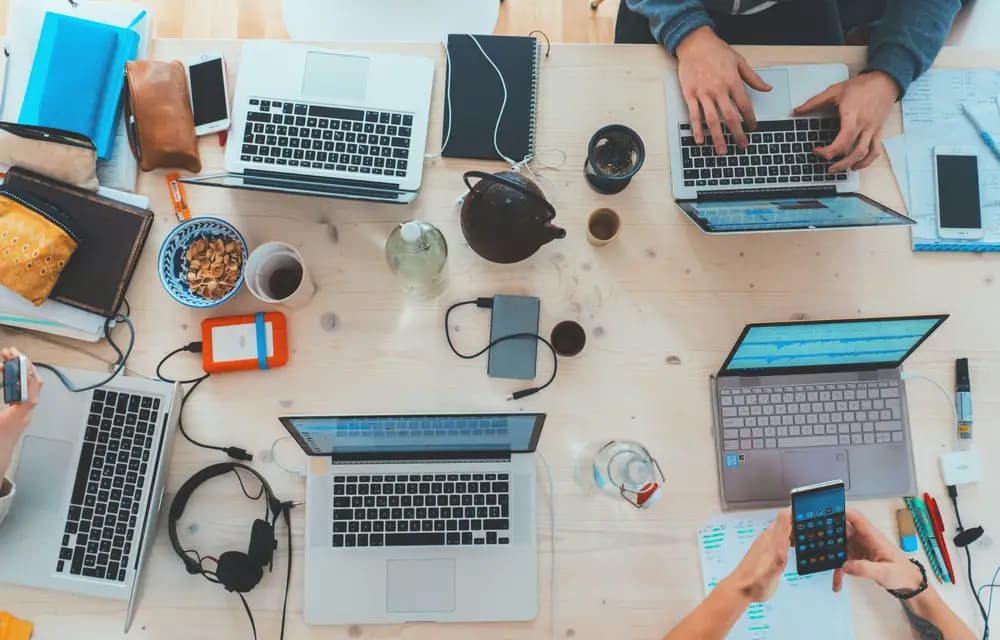An overhead view of laptops, notebooks and phones on a shared desk