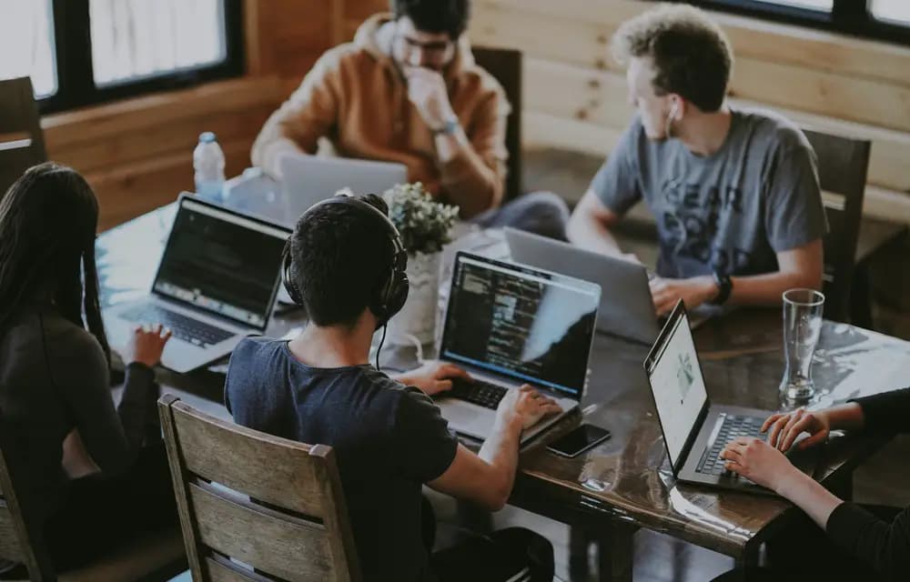 A small team working on laptops around a wooden table