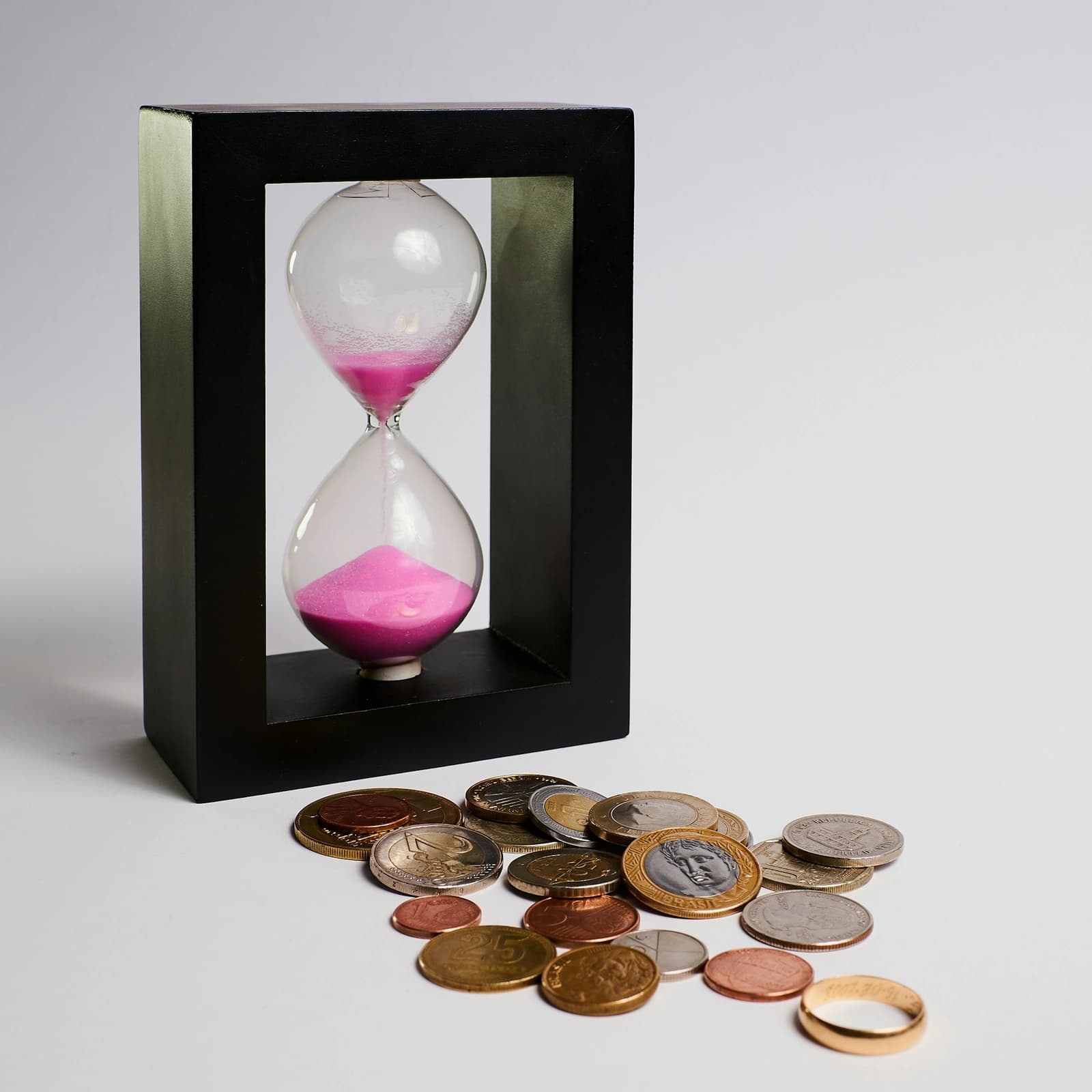 An hourglass beside a pile of coins