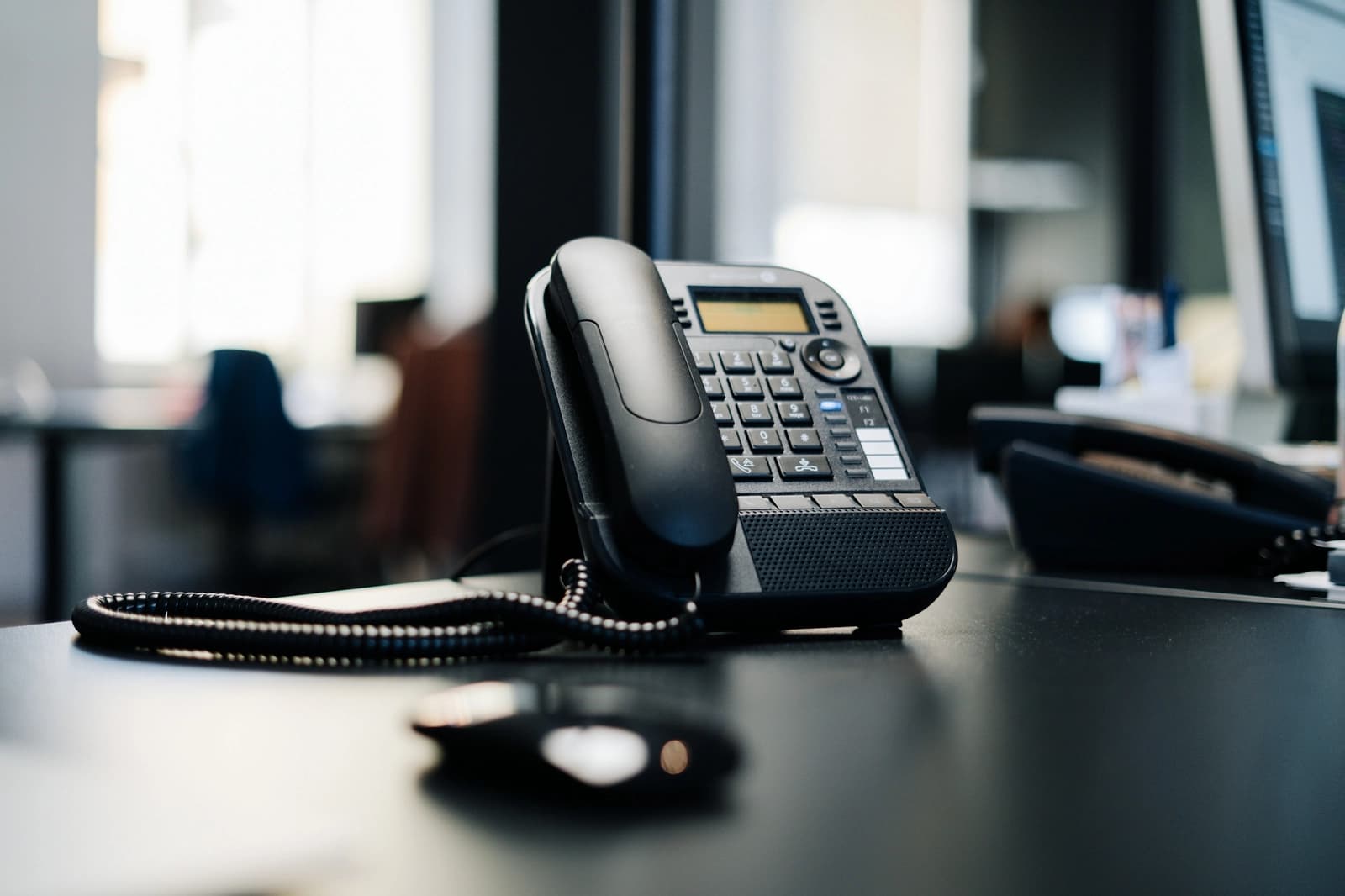 A business desk phone on a dark desk in an office