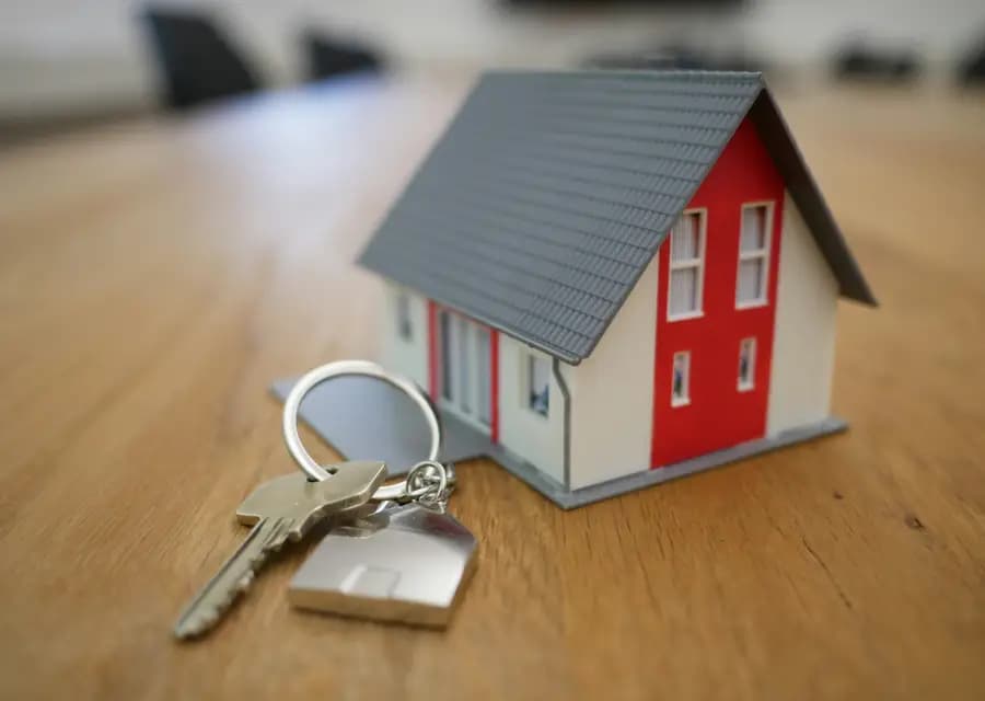 A miniature house and keys on a wooden desk