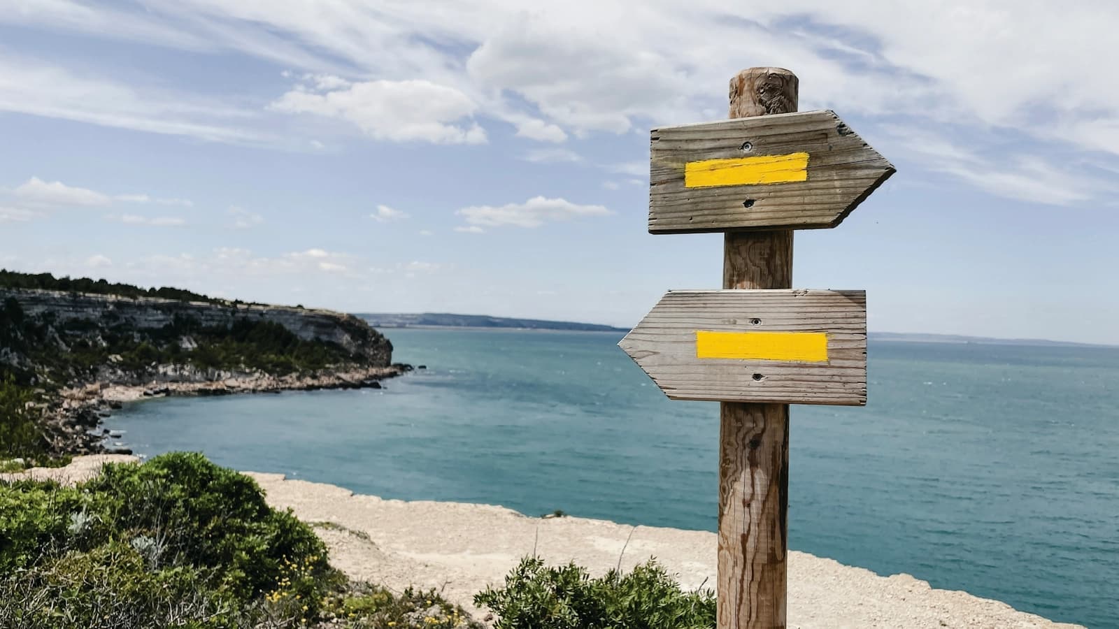 A wooden signpost with two arrows pointing in different directions by the sea